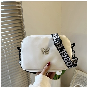Detail of white nylon crossbody bag with butterfly pendant and printed wide strap
