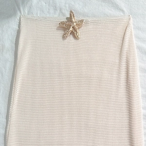 Detail of cream knit beach skirt showing textured fabric and golden starfish charm
