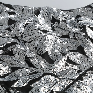 Vue macro de paillettes argentées et broderies florales sur tissu de robe de soirée noir
