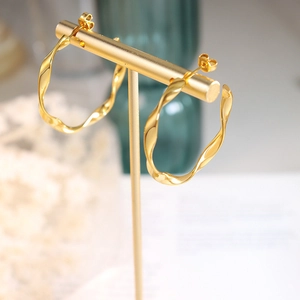 Twisted gold hoop earrings in C-shape design displayed on a professional jewelry stand