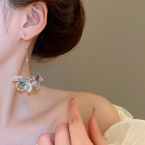 Close-up of model wearing silver chain floral earrings with clear petals and blue stones