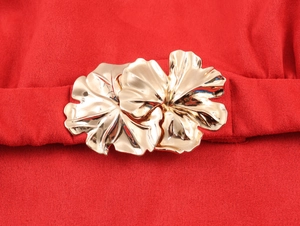 Gros plan d'une boucle fleurie en métal doré sur une robe en daim rouge avec ceinture