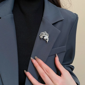 Dettaglio della spilla a piuma in argento con perla e zirconi su un abito grigio