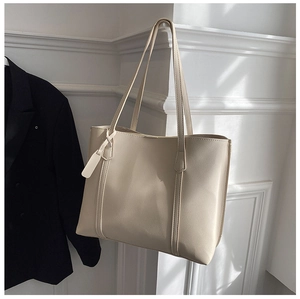 Detail of a beige PU leather tote bag hanging on a minimalist white wall with soft lighting