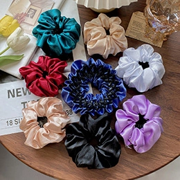 Flat lay of colorful velvet and silk scrunchies on a wooden table with lifestyle props