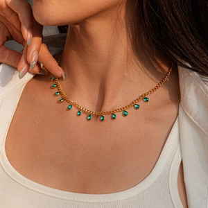 Close-up of a gold sweater chain with green teardrop gemstones on a female model