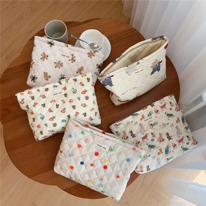 Detailed overhead shot of five quilted cotton makeup bags with cute bear prints on a wood table