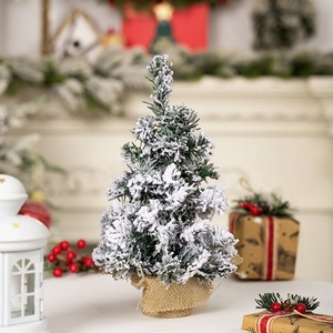 Miniature snow-flocked Christmas tree with burlap base in a cozy festive setting