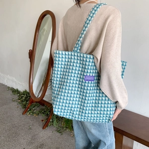 Blue and white plaid woven tote bag with purple label shown on shoulder by model