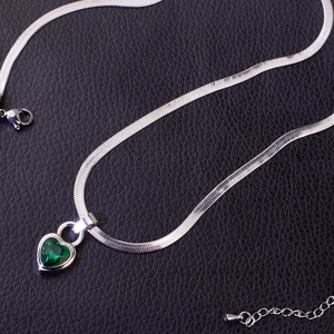 Macro detail of the heart-shaped emerald pendant on a silver flat snake chain