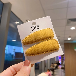 Close-up of two yellow cashmere-like teardrop hair clips with beaded edges on a card