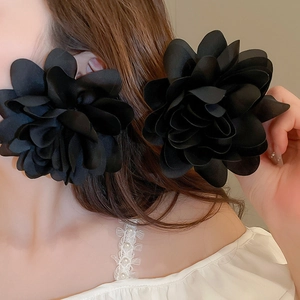 Close-up of large black fabric 3D petal earrings in a statement vacation style