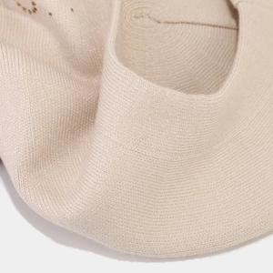 Dettaglio del berretto in maglia beige con trama a coste sottili e rivetti metallici