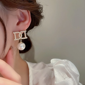 Detailed close-up of French-style pearl earring with golden letter D frame and large drop