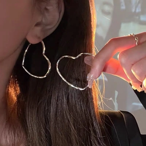 Minimalist silver heart hoop earrings with polished metal finish worn by a model