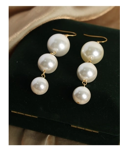 Detail of three pearl drop earrings with gold finish on green velvet and gold satin