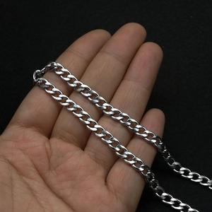 Close-up of silver Cuban link chain held by hand against a black background