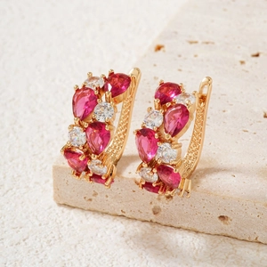 Close-up of gold-plated earrings with red teardrop stones on a minimalist stone surface