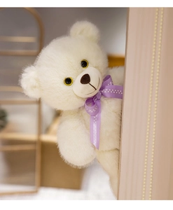 Close-up of fluffy white teddy bear with purple bow peaking from behind a wood plank