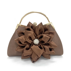 Detalle de bolso de satén marrón con flor 3D y asa de metal dorado para fiestas