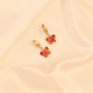 Gros plan de boucles d'oreilles papillon dorées avec cristaux orange sur soie beige
