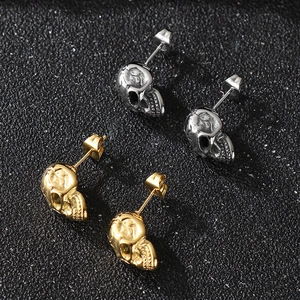 Close-up of gold and silver stainless steel skull stud earrings with vintage texture