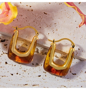 Detail of amber resin and gold U-shaped earrings on stone background with petals