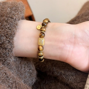 Detail of tiger eye beaded bracelet with gold hollow pendant on a model wrist