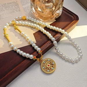 Double-layer pearl necklace with gold hollow pendant and red gemstone on a wooden tray