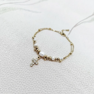 Macro detail of gold-plated pearl bracelet with a sparkling rhinestone cross pendant