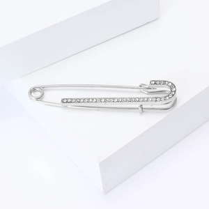 Detail of silver alloy brooch pin featuring clear rhinestones on white geometric base