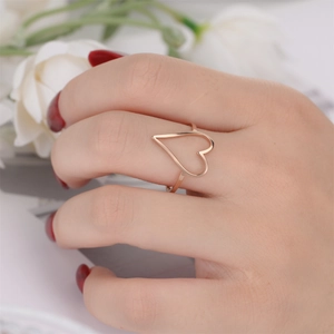 Close-up of a rose gold hollow heart ring on finger with elegant floral background