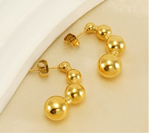 Macro di orecchini a forma di pisello in acciaio inossidabile placcato oro 18k su seta champagne