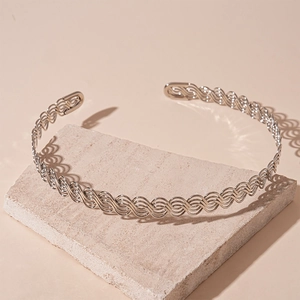 Detailed view of silver wave woven metal collar necklace on a textured stone surface