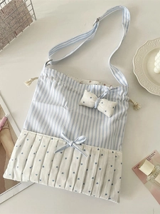 Blue striped crossbody bag with bow accents and drawstring on a white desk