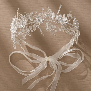 Elegant silver bridal headband with crystal flowers and pearls on beige background