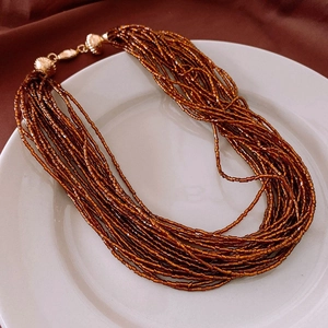 Detail view of multi-strand beaded necklace with gold clasp on white ceramic plate