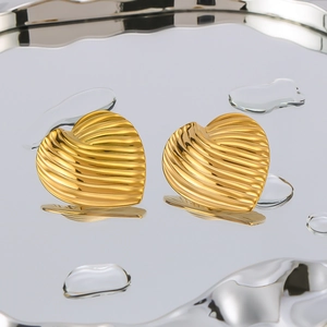 Golden heart earrings with textured stripes on a reflective mirror surface with water drops