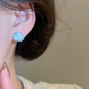 Detail of light blue crystal flower stud earring worn on ear with soft petals