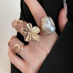 Detail view of a set of golden flower rings with irregular pearls on a model hand