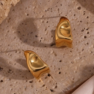 Macro view of gold irregular liquid metal style earrings on a beige stone background
