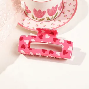 Macro detail of pink acrylic hair claw clip with red heart patterns on white background