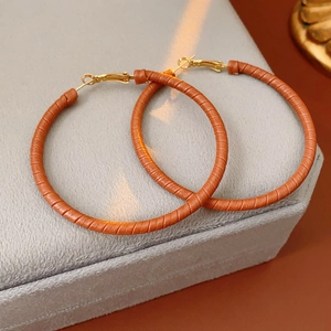 Close-up of brown leather wrapped gold hoop earrings on a grey velvet jewelry pad