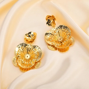 Fashionable golden layered flower petal earrings displayed on elegant beige silk fabric