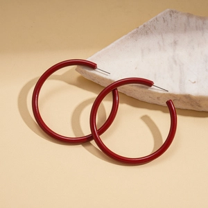 Detail view of red C-shaped acrylic hoop earrings on minimalist marble surface