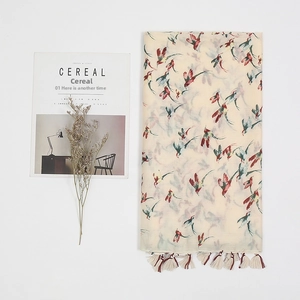 Detail of red and cyan bird print on a beige cotton-linen scarf with fringed edges