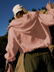 Outdoor back view of a pink long sleeve hooded sweatshirt with a casual drawstring design