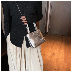 Silver handbag with 3D bow details and metal chain strap worn by a model