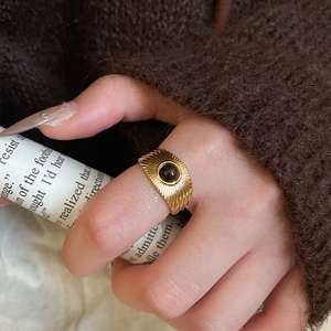 Macro shot of a gold eye-shaped ring featuring a black gemstone inlay on a finger