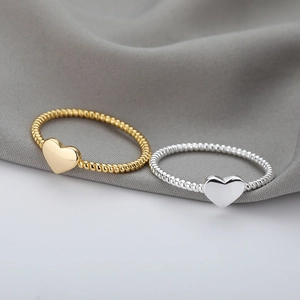Gold and silver heart rings with twisted band texture on soft grey fabric background